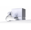 A clear glass perfume bottle with a transparent cap sits in front of a metallic silver box embossed with the brand name 'GINA SANDRINI' on a clean white background.